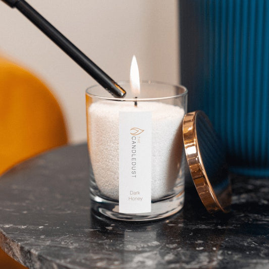 1. Candledust powdered candle in glass, Dark Honey scent, being lit on a marble surface with rose gold lid