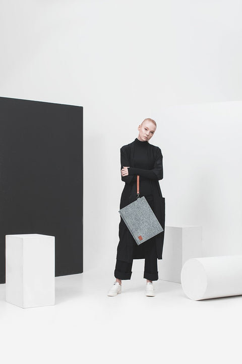 1. Woman holding Nordhale Berg 13'' grey laptop bag with removable wristband in minimalist studio setting
