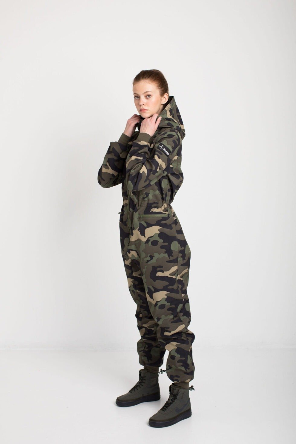 4. Women's SUSANNA softshell overall by Nuckö, adjusting hood, side view in studio
