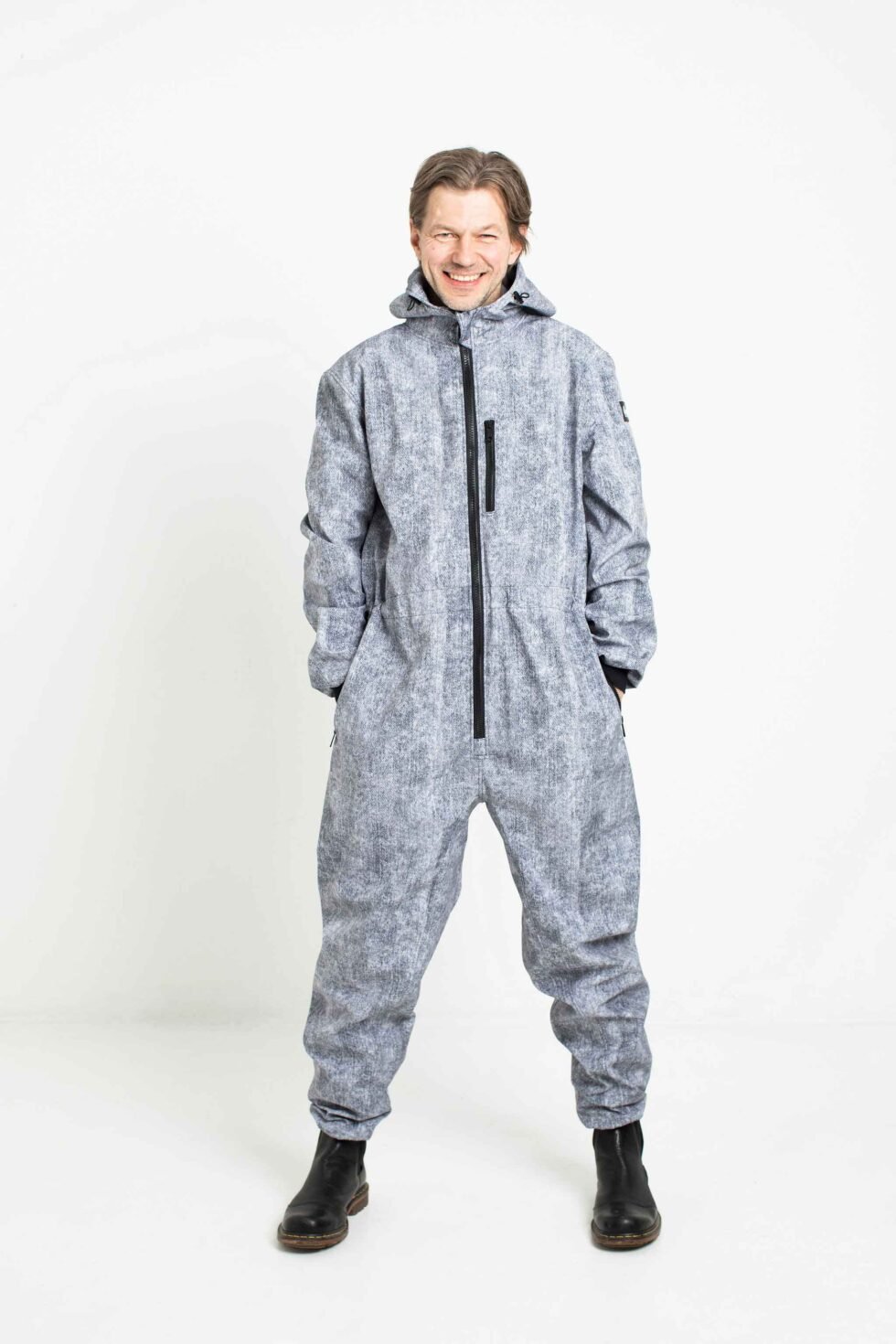 1. Man wearing grey Nuckö MEELIS softshell overall with adjustable hood and waist, standing in studio setting