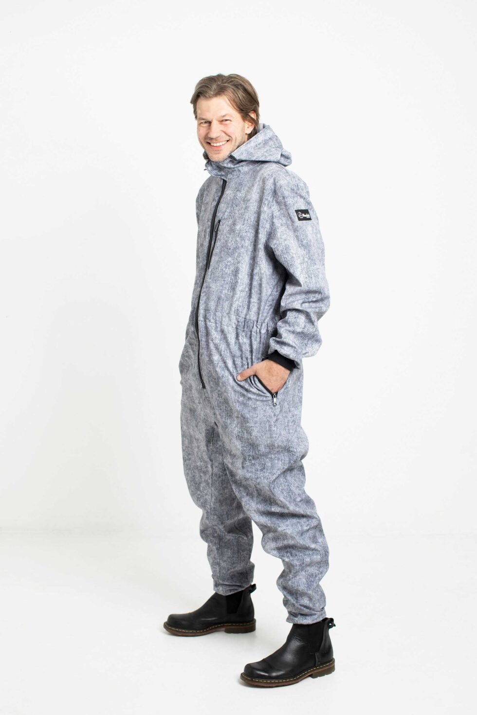 3. Side view of man in grey Nuckö MEELIS softshell overall with hands in pockets, studio setting