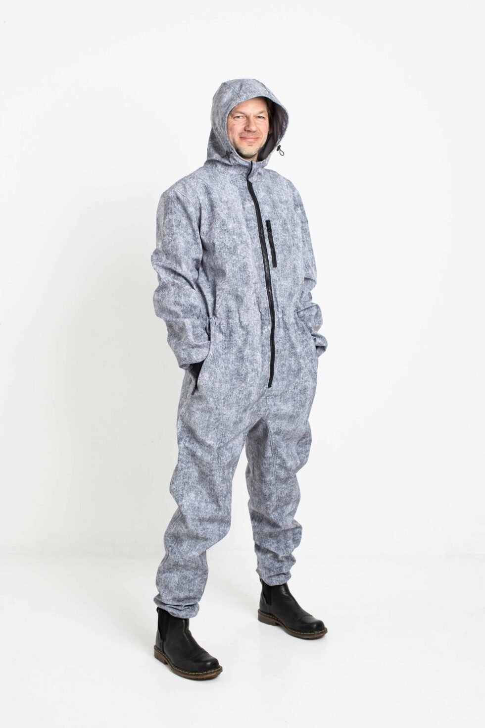 2. Man in grey Nuckö MEELIS softshell overall with hood up, hands in pockets, studio background