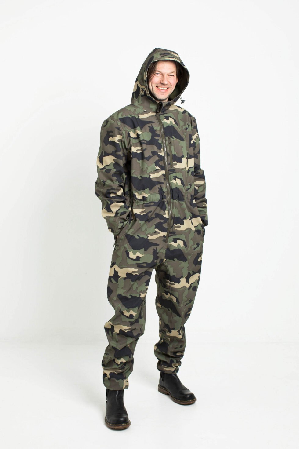 4. Man smiling in Nuckö RINGO softshell overall with hood up in camouflage pattern in studio