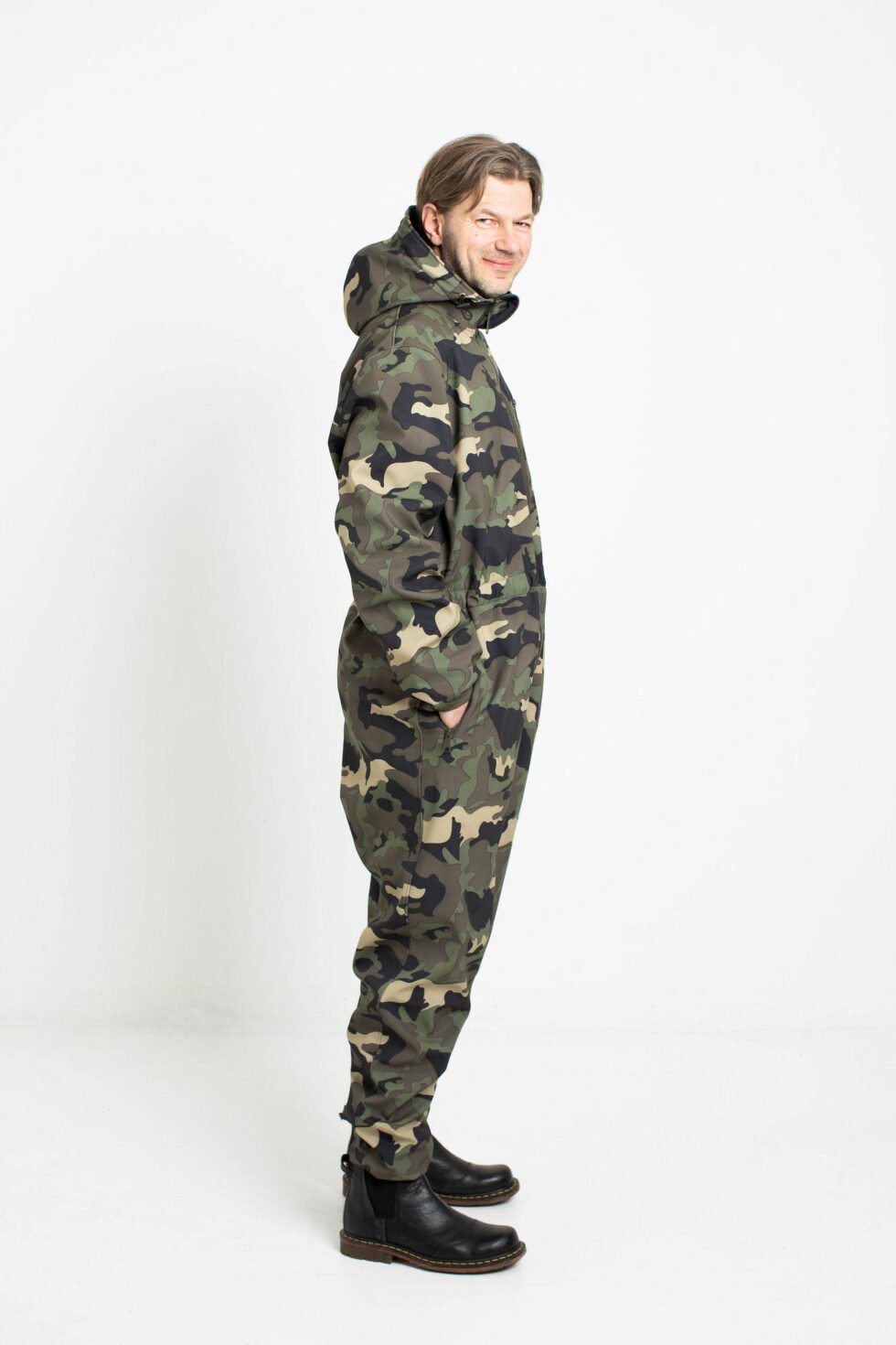 2. Side view of man in Nuckö RINGO softshell overall with hood up in camouflage pattern in studio