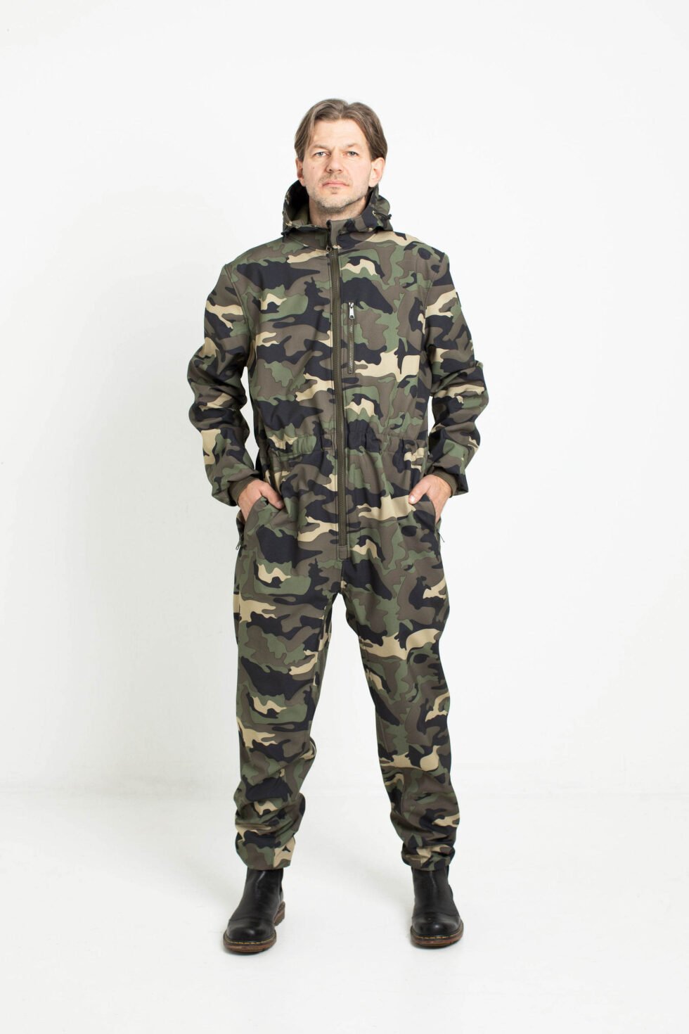 1. Man wearing Nuckö RINGO softshell overall in camouflage pattern standing with hands in pockets in studio setting