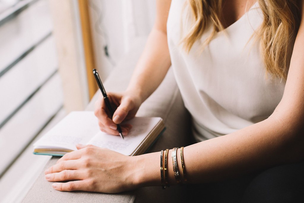 2. Woman writing in a journal wearing Olla RAKAS MUMMI bracelets in silver, rose gold, and gold
