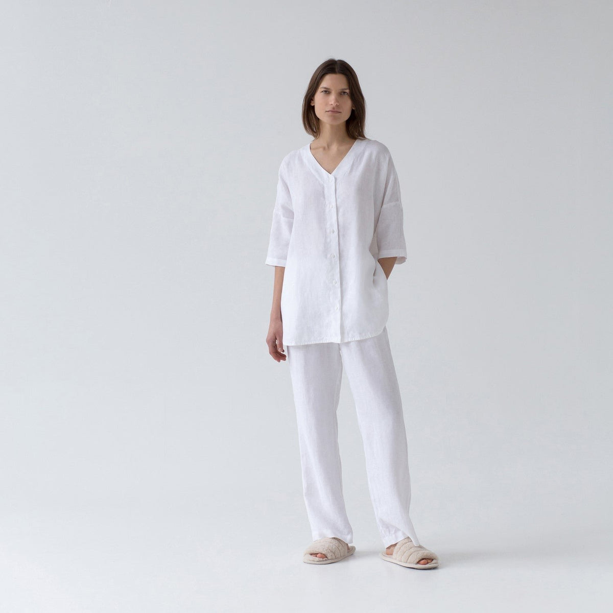 1. Woman wearing optical white linen loungewear set with V-neck shirt and relaxed pants in a studio setting