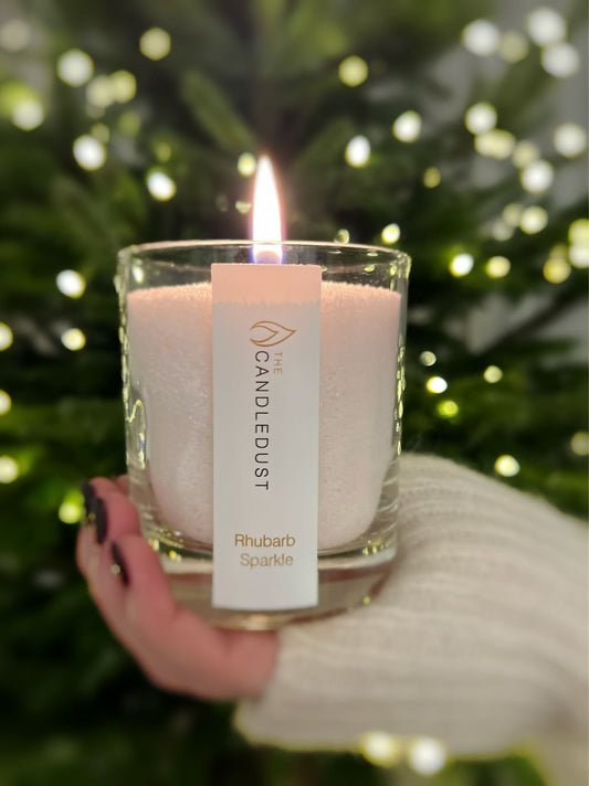 2. Candledust Rhubarb Sparkle powdered candle lit in glass, held by a person in front of a tree