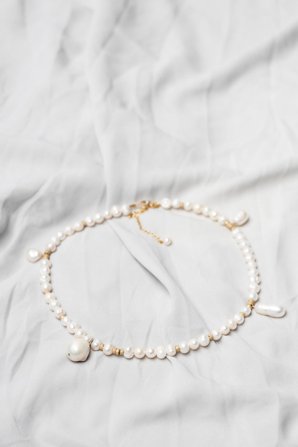 3. Flat lay of New Vintage by Kriss custom-made pearl necklace showcasing Baroque pearls and gold-filled details on a light fabric