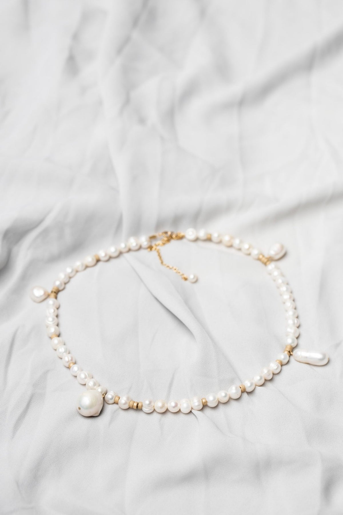 3. Flat lay of New Vintage by Kriss custom-made pearl necklace showcasing Baroque pearls and gold-filled details on a light fabric