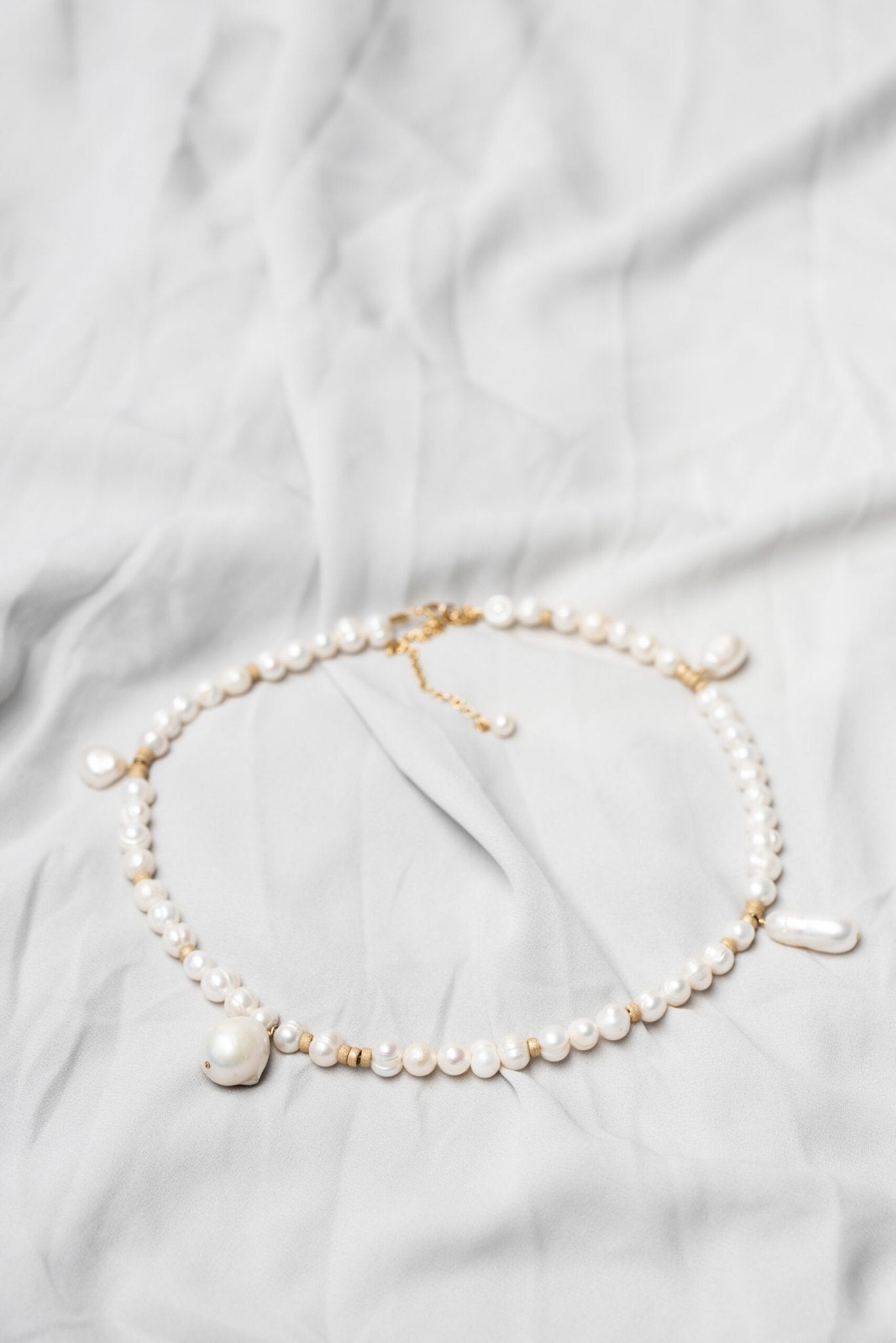 3. Flat lay of New Vintage by Kriss custom-made pearl necklace showcasing Baroque pearls and gold-filled details on a light fabric