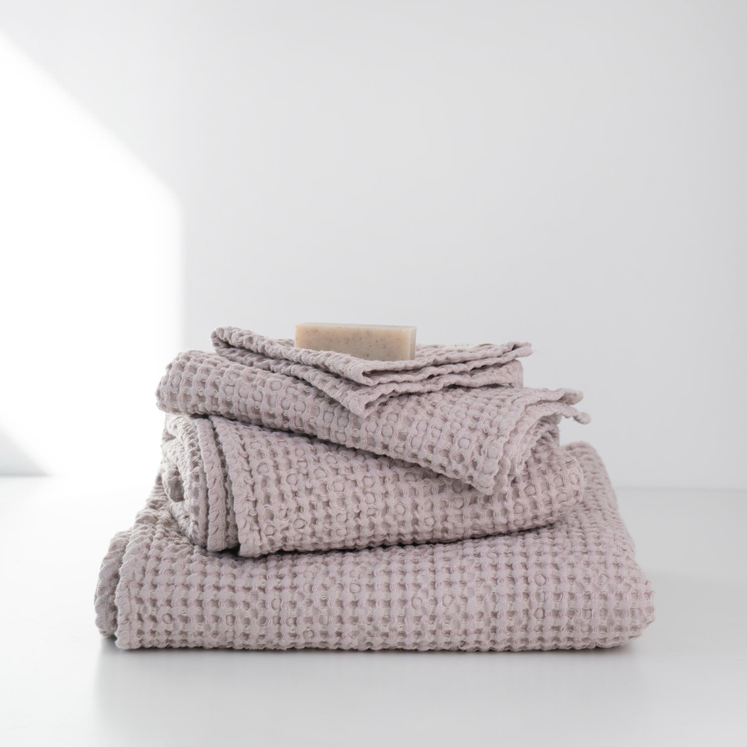 1. Stack of powder-colored honeycomb waffle towels with a bar of soap on top, set against a white background