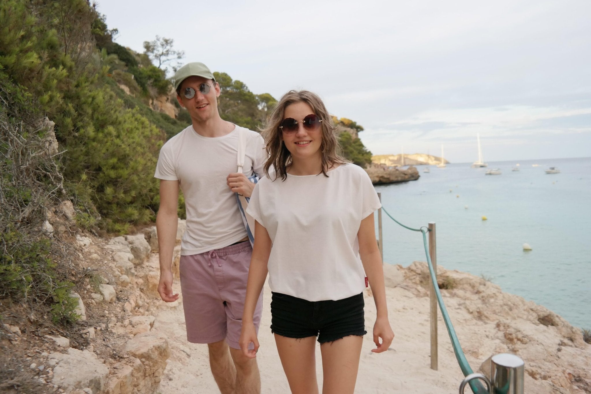 1. Woman wearing Smarttan Tan-Through T-Shirt in coral, walking on a beach path with a man, showcasing outdoor lifestyle
