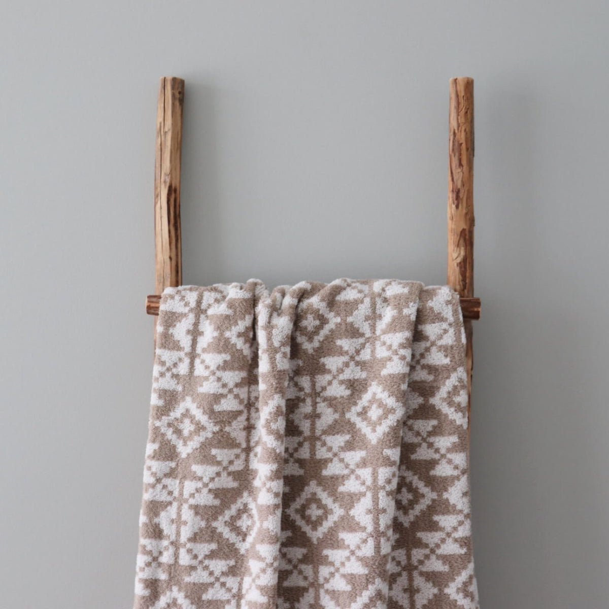 1. Beige and white terry sauna towel with Harju County mitten pattern draped over wooden ladder against grey wall