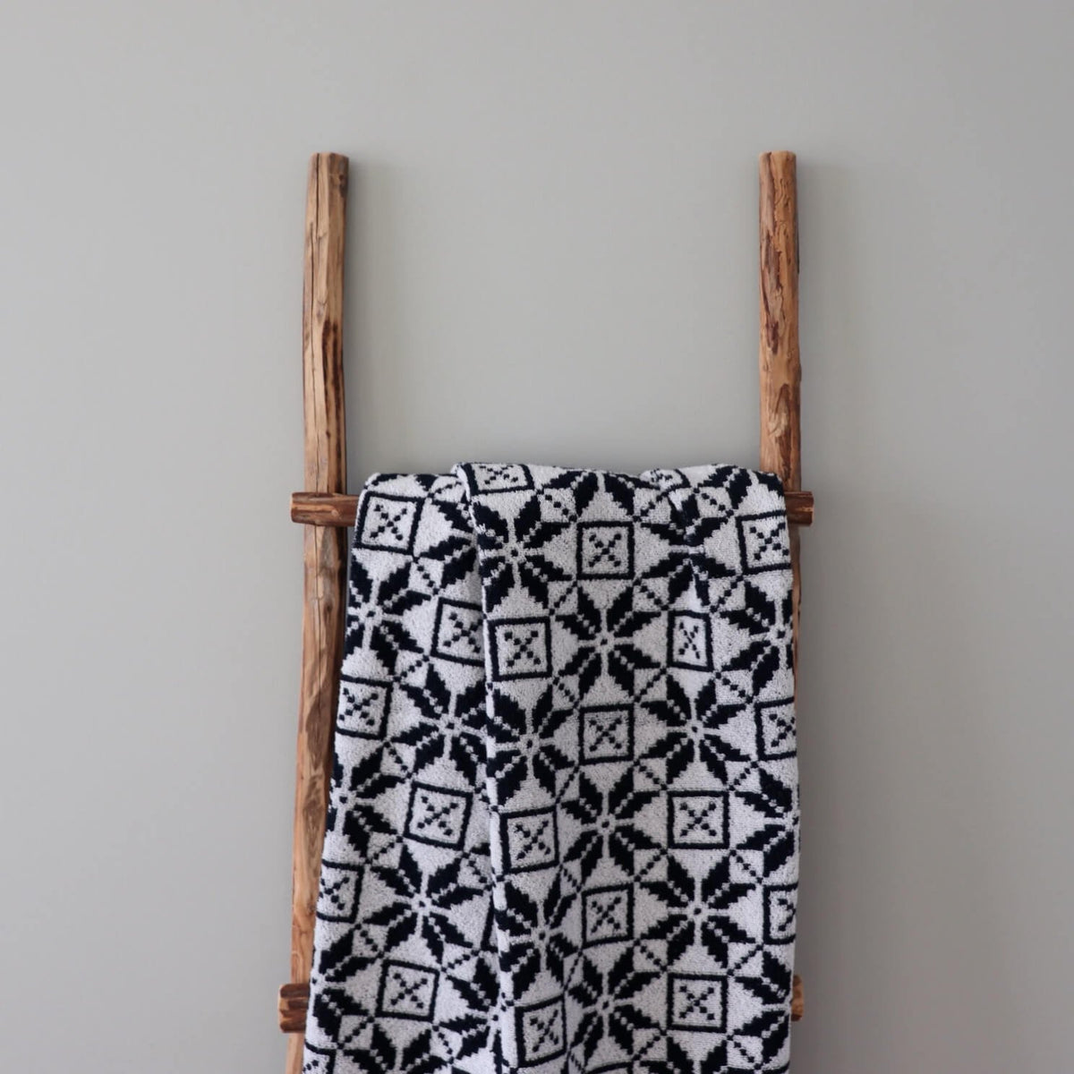 2. Black and white sauna towel featuring Hiiumaa mitten pattern hanging on rustic wooden ladder