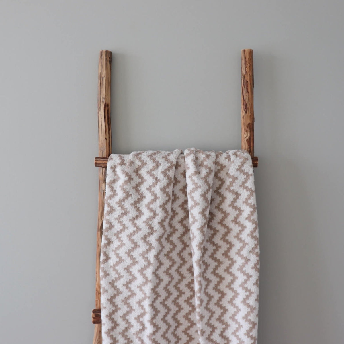 1. Beige and white terry sauna towel with Tartu County mitten pattern draped over a rustic wooden ladder against a neutral wall