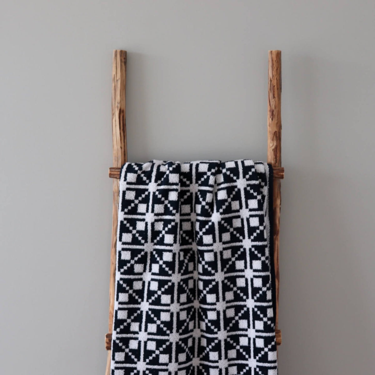 1. Black and white sauna towel with Virumaa mitten pattern draped over wooden ladder against grey wall