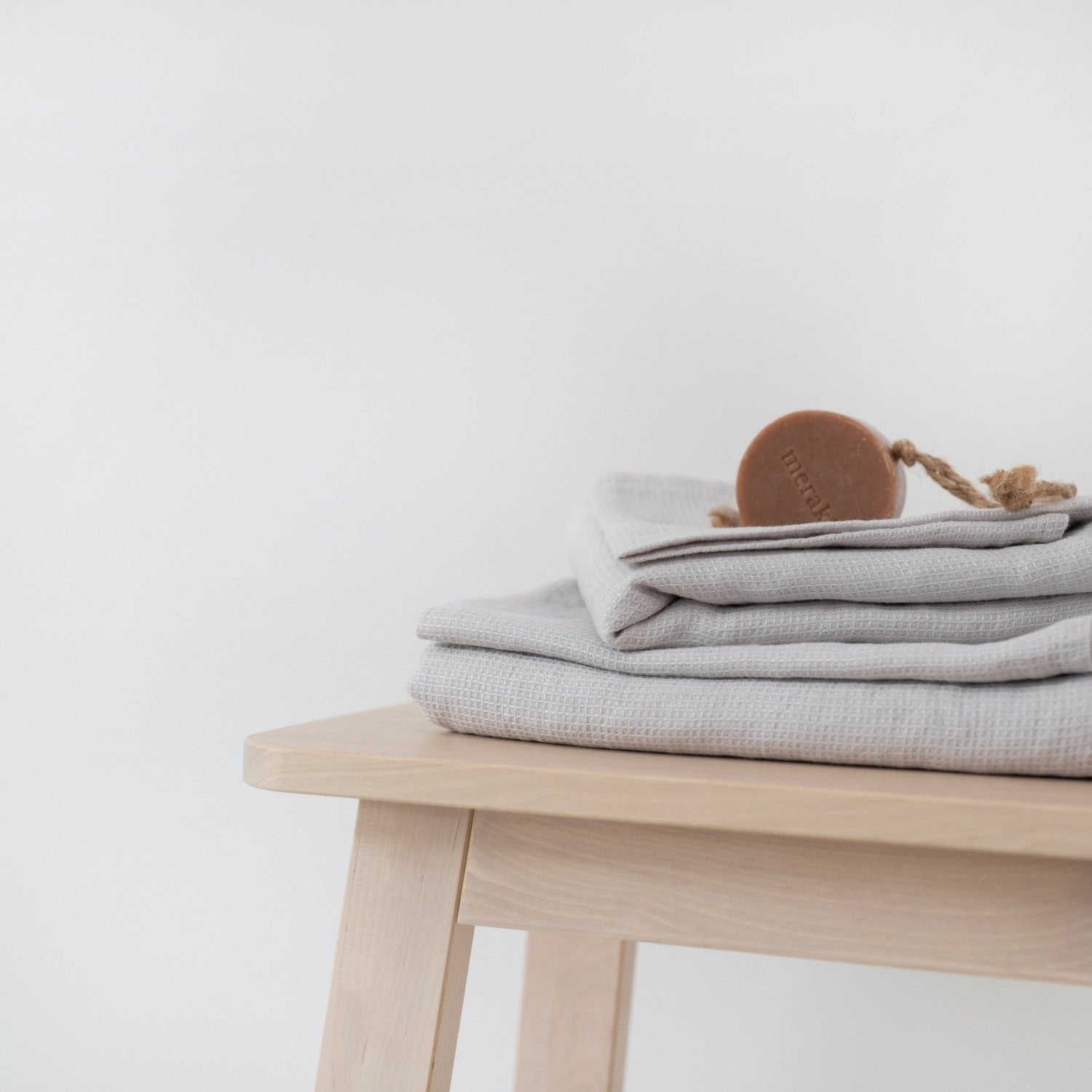 1. Silver linen fine waffle towel folded on wooden stool with round soap on top, minimalist setting