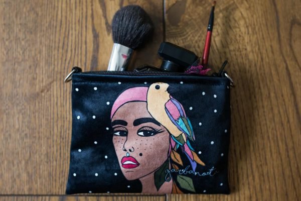 3. Garbanota black makeup bag with artistic print, displayed on chair with denim jacket and sunglasses