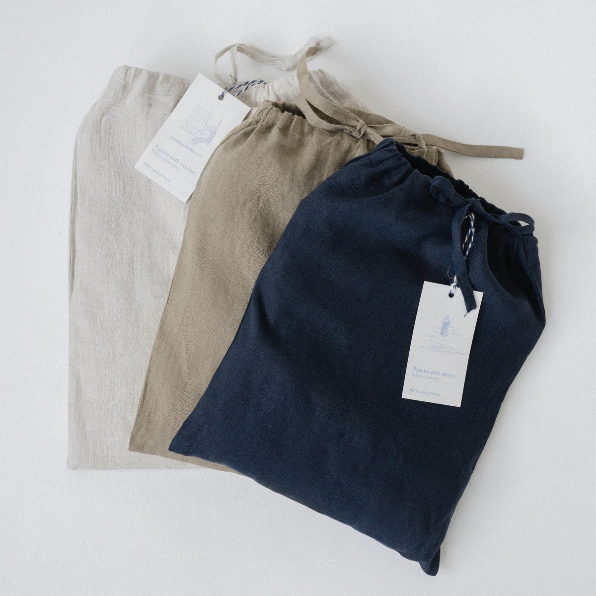 4. Flat lay of three linen bags in beige, tan, and navy, each with a tag, on a white background