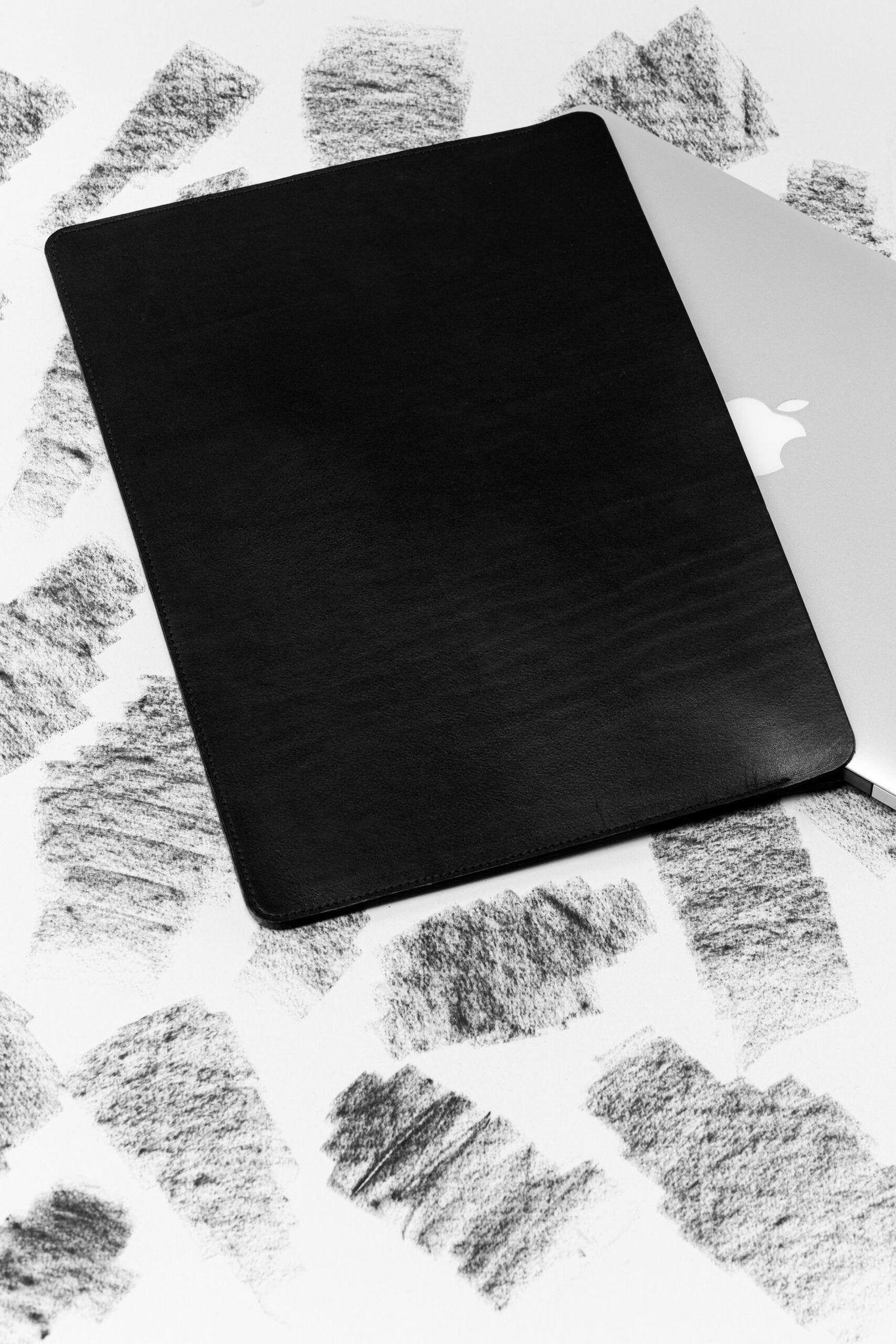 2. Black leather laptop sleeve with laptop partially inserted on textured background