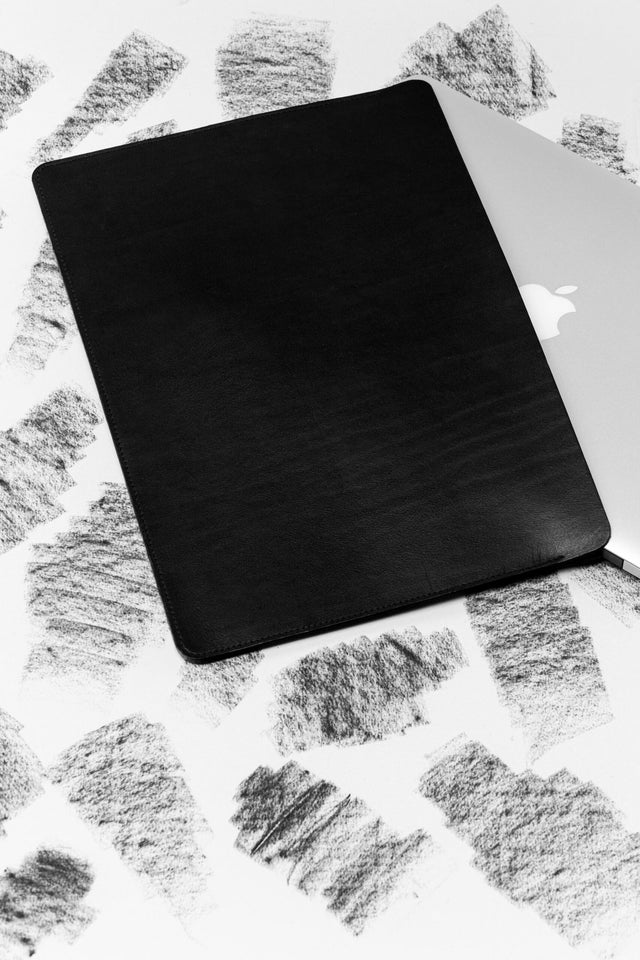 2. Black leather laptop sleeve with laptop partially inserted on textured background