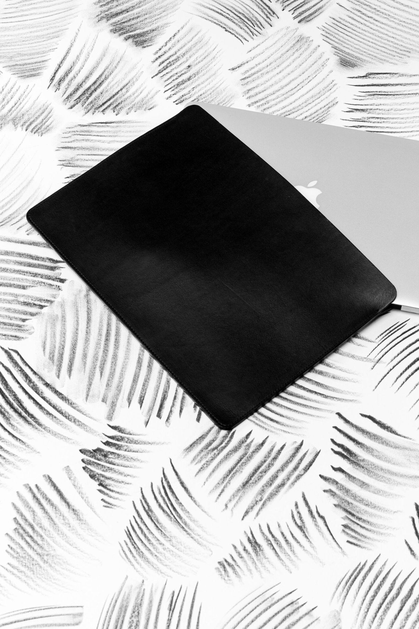 3. Black leather laptop sleeve with laptop on abstract patterned surface