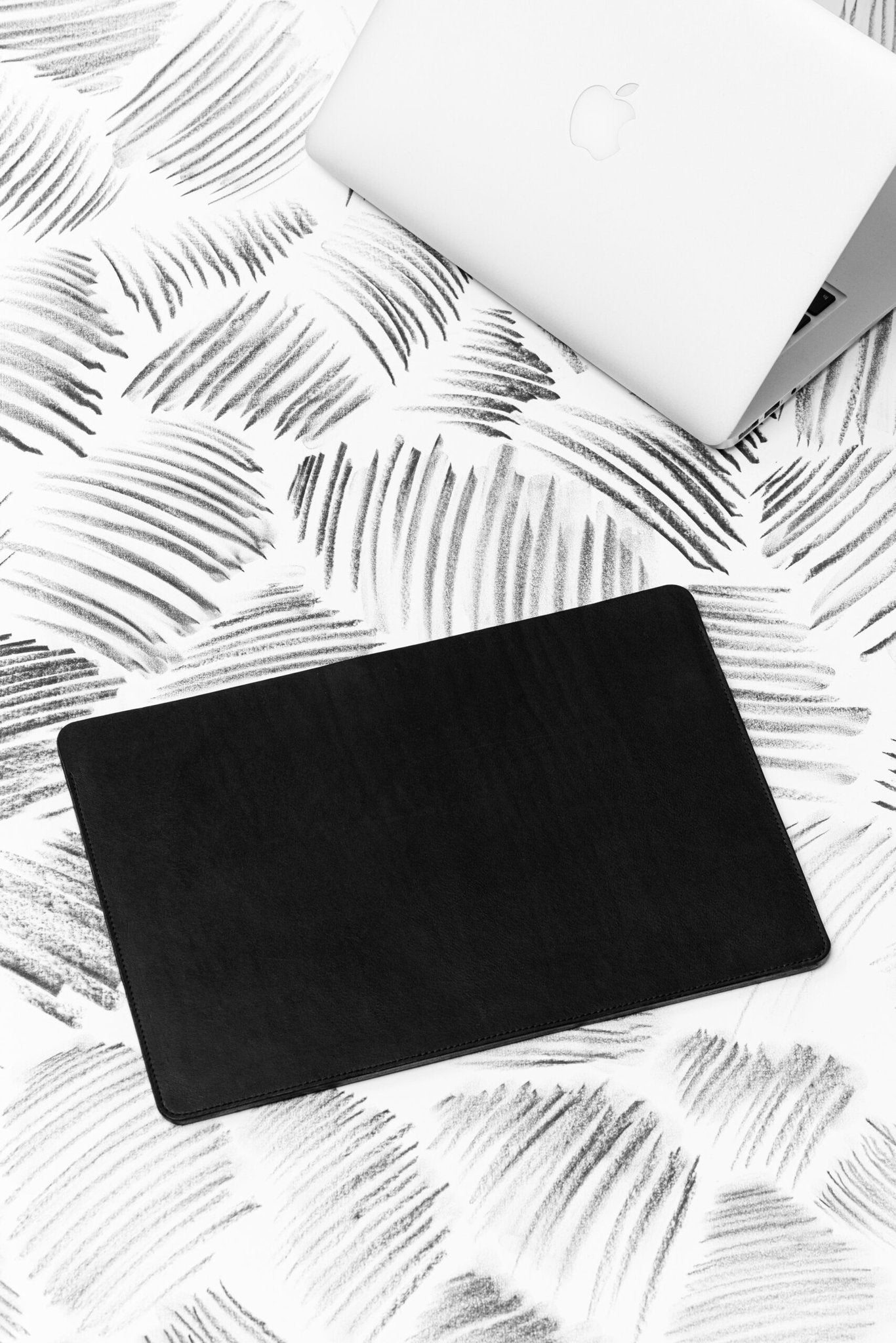 1. Black leather laptop sleeve on patterned surface with partially visible laptop