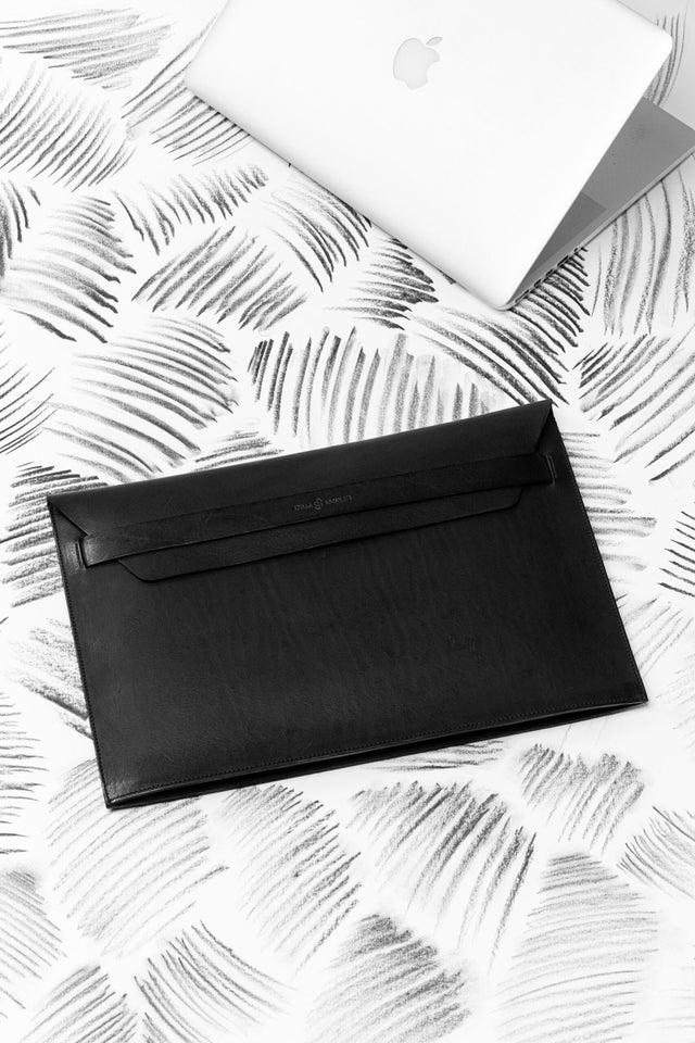 3. Black Stella Soomlais leather laptop sleeve with flap on patterned surface beside a closed laptop