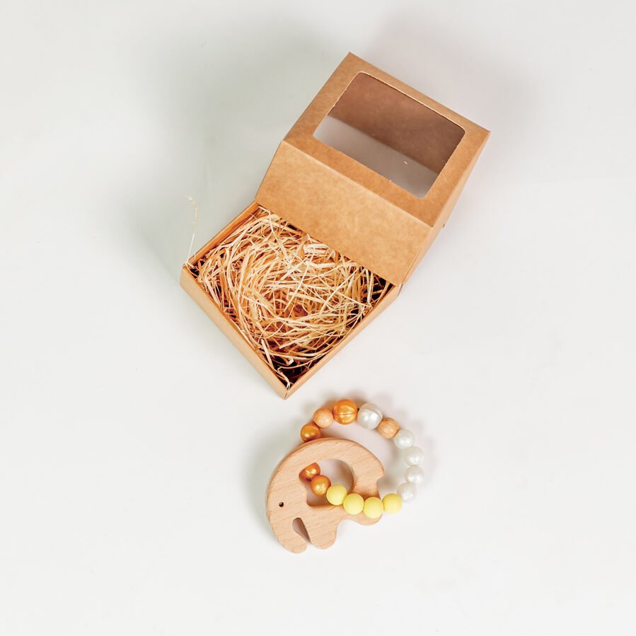 2. Amber silicone baby teether-bracelet with wooden elephant next to open brown gift box on white background
