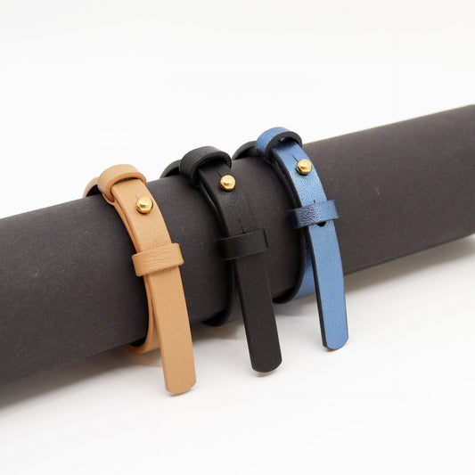 2. Trio of leather bracelets in black, tan, and blue with brass fasteners displayed on a roll
