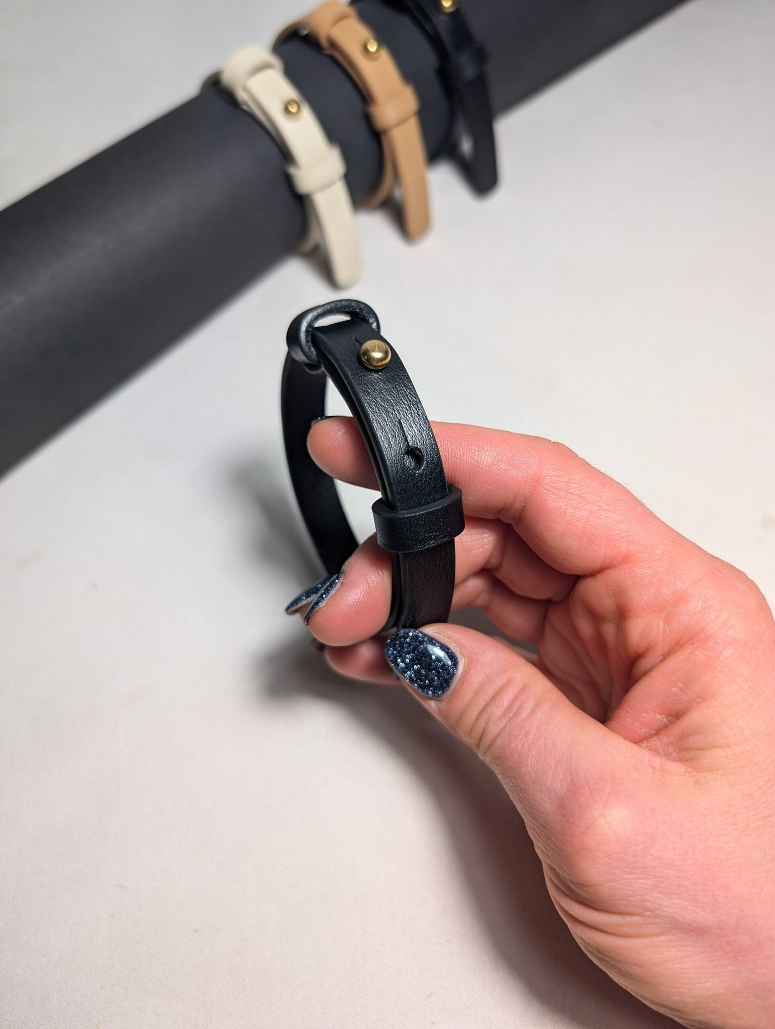 4. Close-up of black leather bracelet with brass fastener held in hand, other colors in background