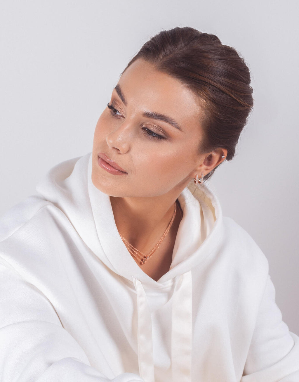 1. Woman wearing MyaMoon Metropolitan Glow White Earrings in rose gold, styled with a white hoodie, showcasing elegant urban fashion
