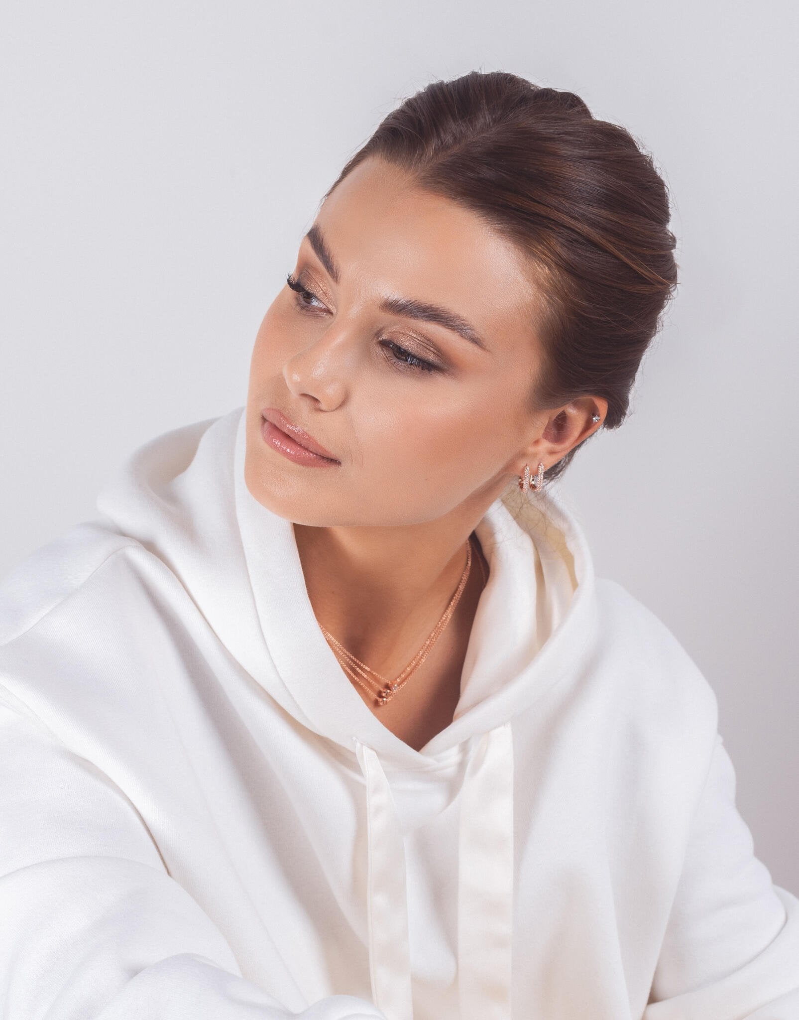 1. Woman wearing MyaMoon Metropolitan Glow White Earrings in rose gold, styled with a white hoodie, showcasing elegant urban fashion