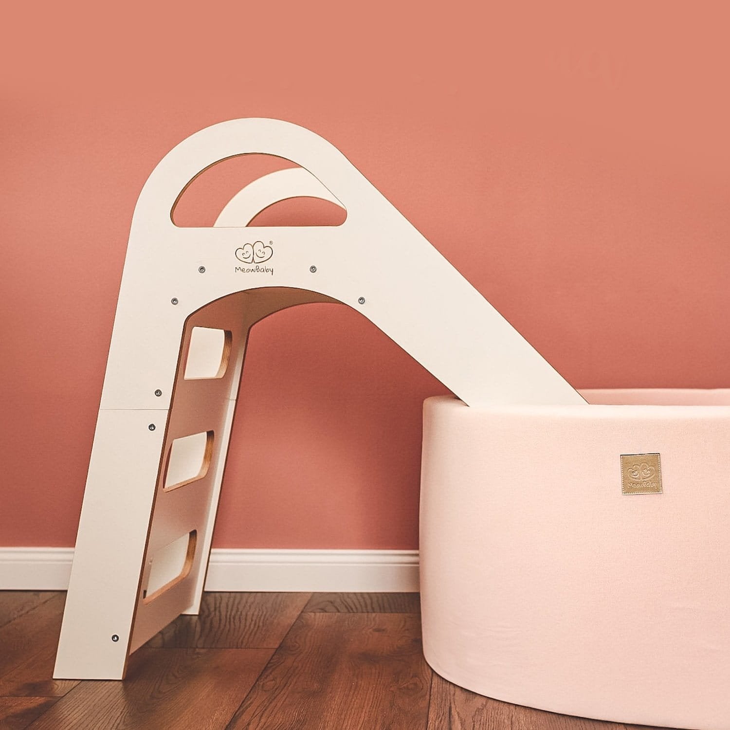 1. Side view of white wooden slide next to a pink ball pit against a coral wall