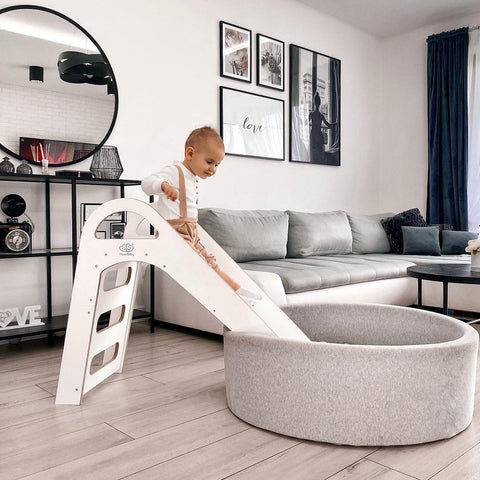 1. Child sliding into a grey ball pit from a white wooden slide in a modern living room