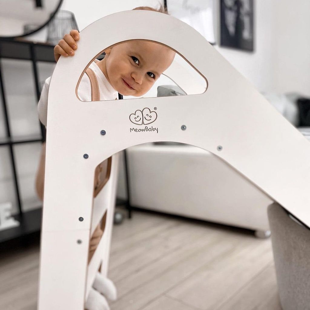 1. Child peeking through the handle of a white wooden slide indoors