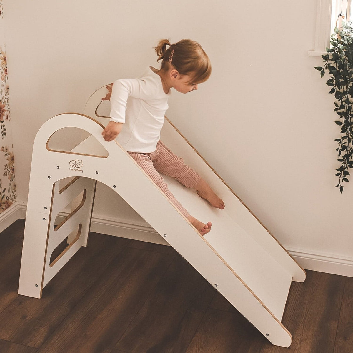 1. Child sliding down a white wooden slide in a room with wooden flooring
