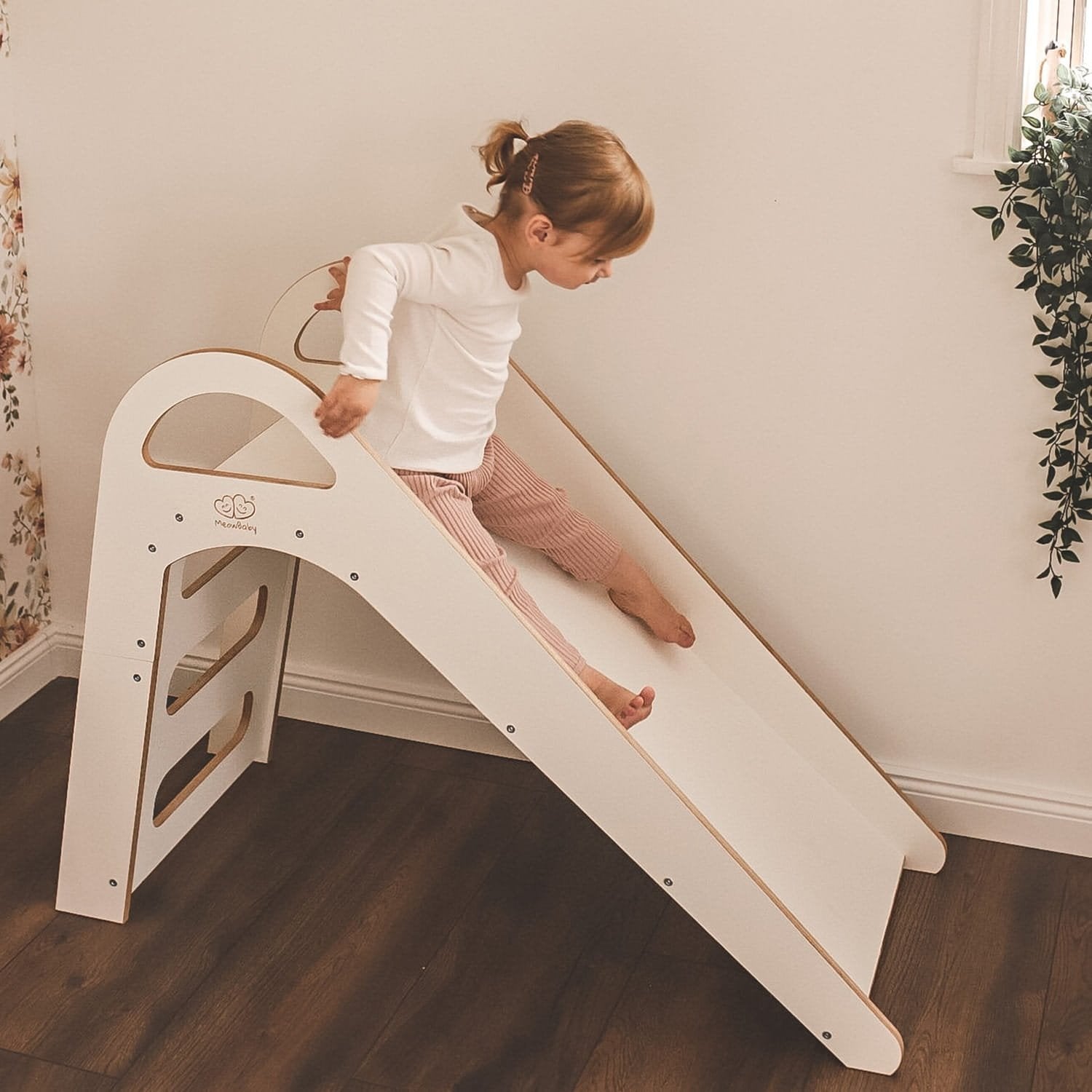 1. Child sliding down a white wooden slide in a room with wooden flooring