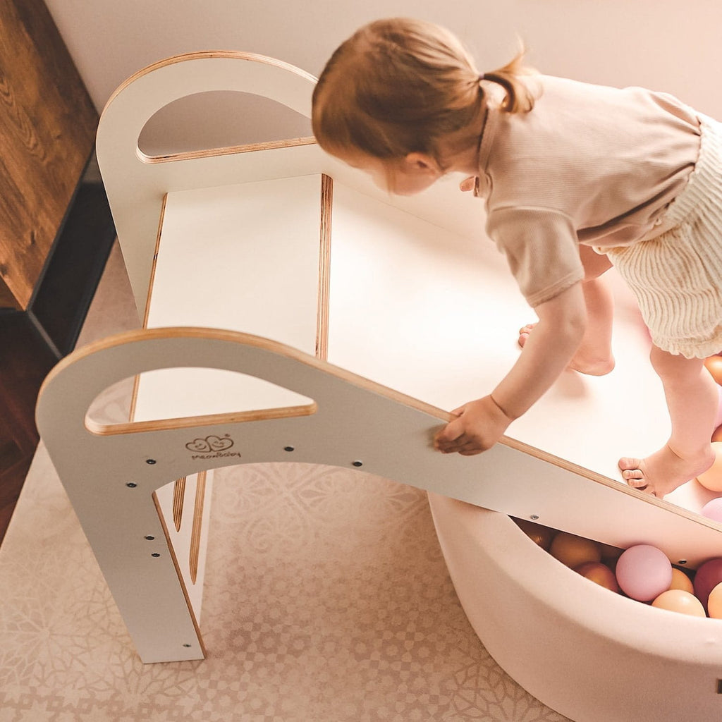 1. Child climbing up a white wooden slide into a ball pit in a playroom