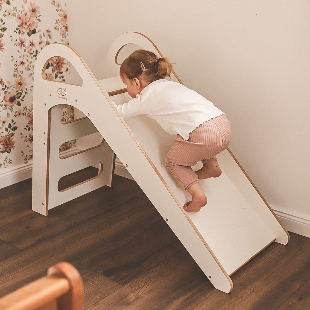 1. Child climbing up a white wooden slide in a room with floral wallpaper