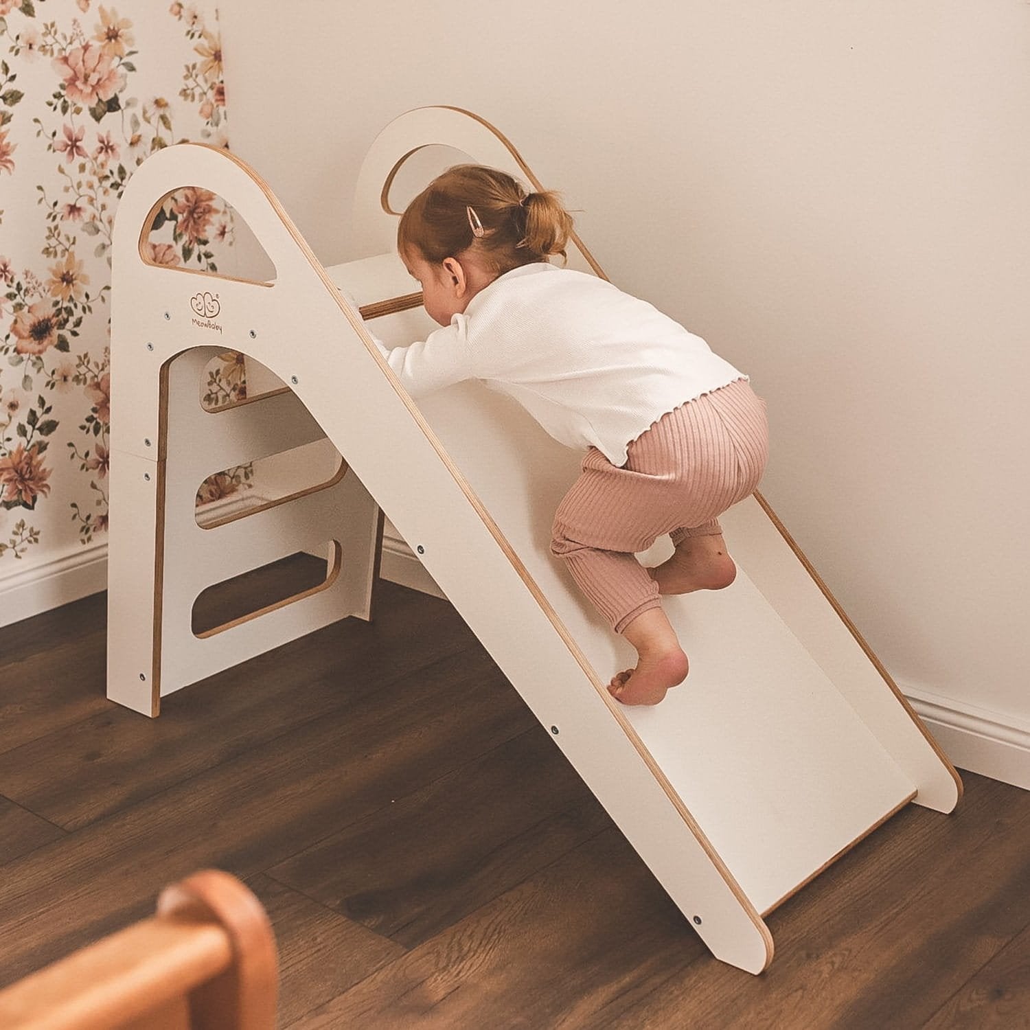 1. Child climbing up a white wooden slide in a room with floral wallpaper