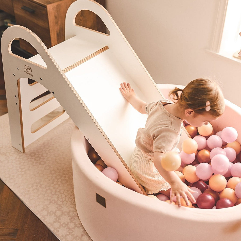 1. Child sliding into a ball pit from a white wooden slide in a playroom