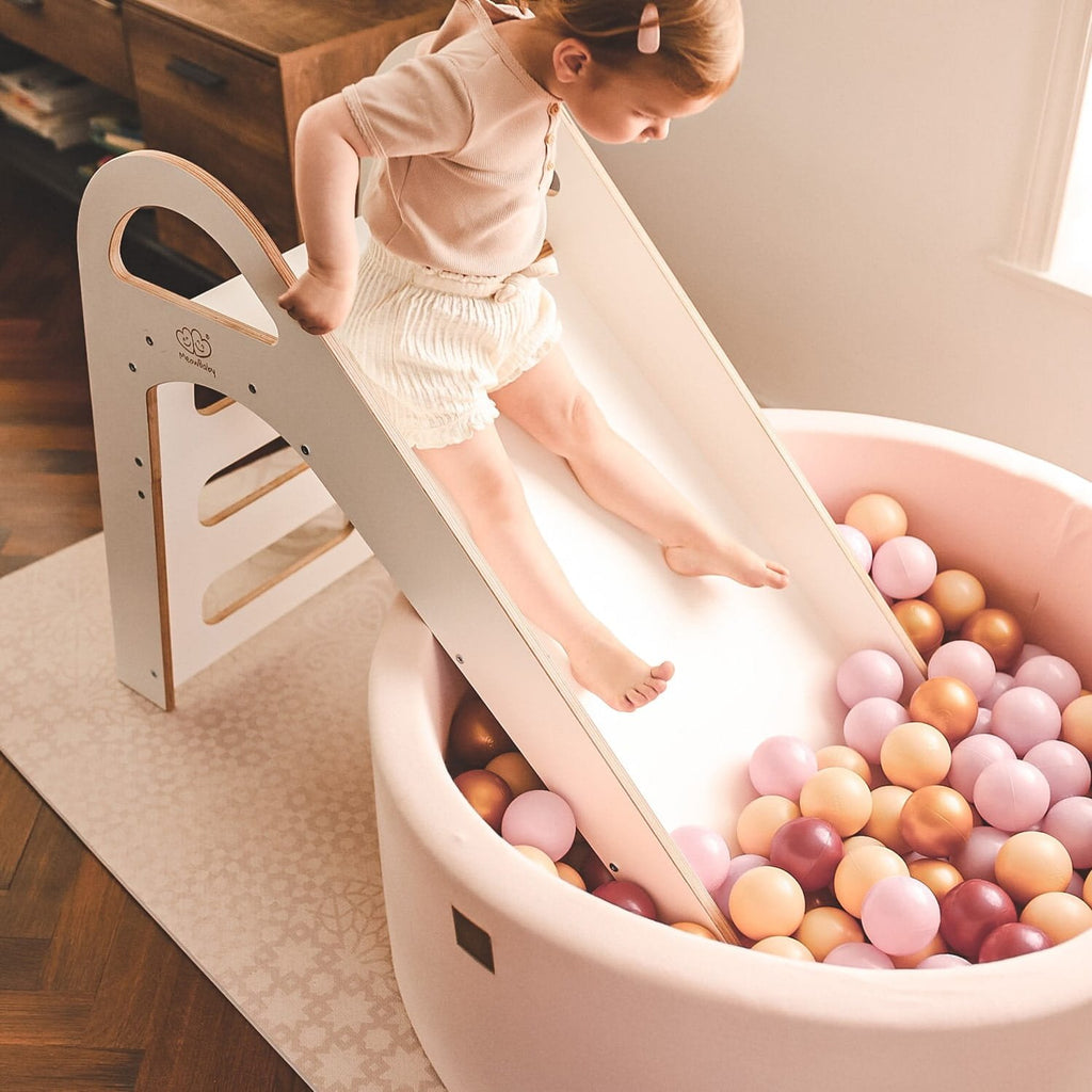 1. Child sliding into a ball pit from a white wooden slide in a playroom