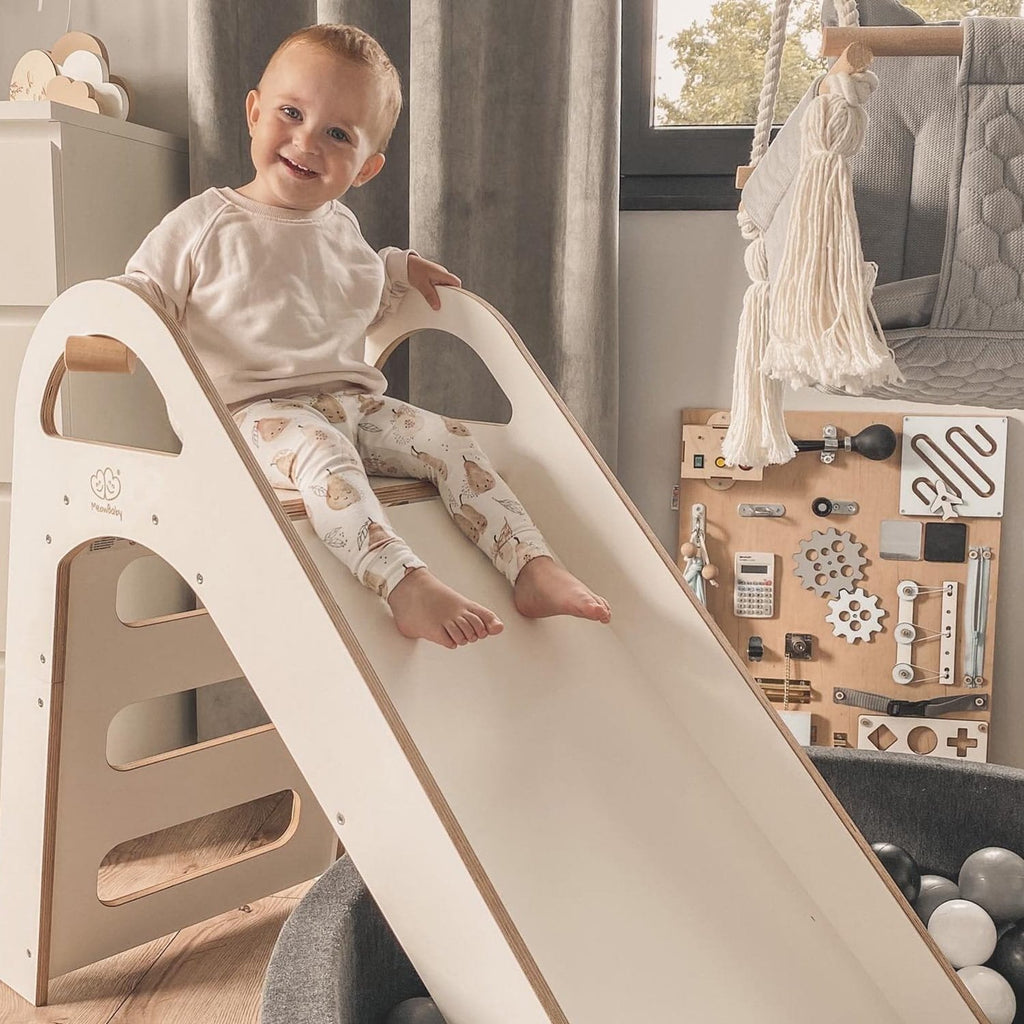 1. Smiling child sitting at the top of a white wooden slide in a playroom