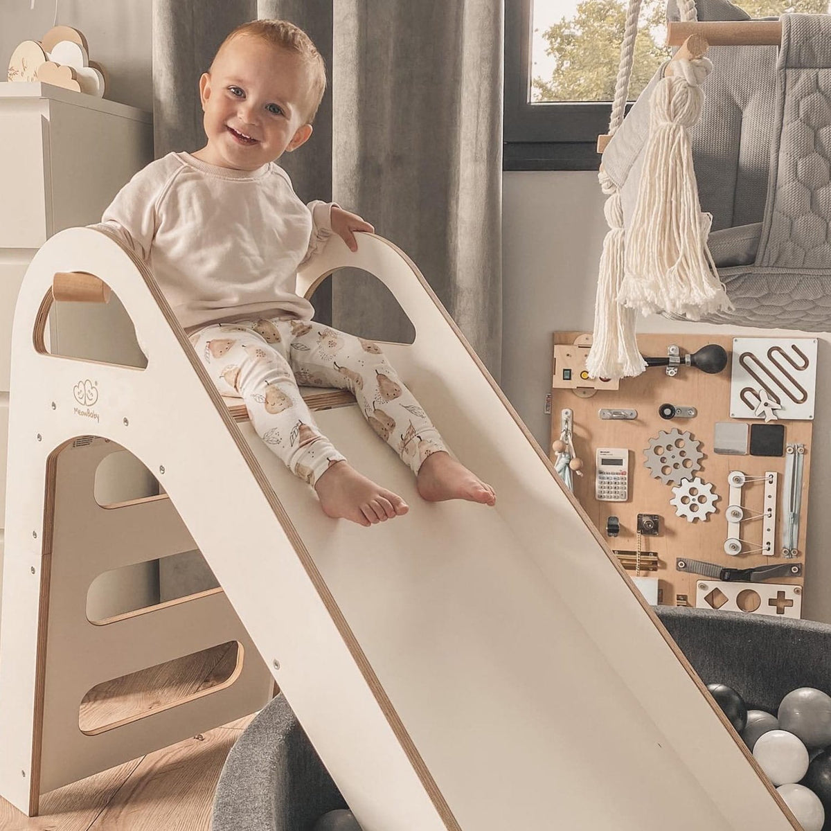 1. Smiling child sitting at the top of a white wooden slide in a playroom
