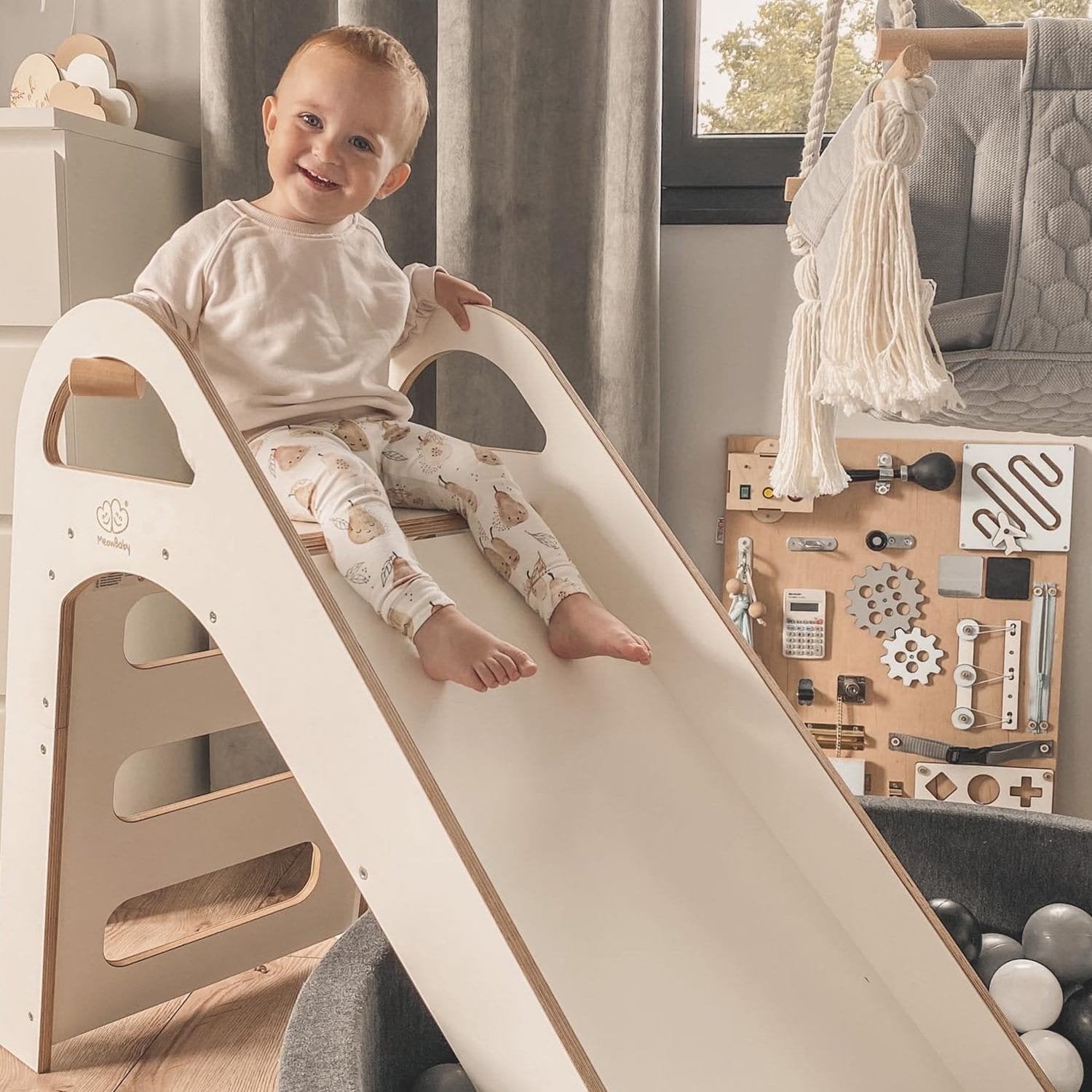 1. Smiling child sitting at the top of a white wooden slide in a playroom