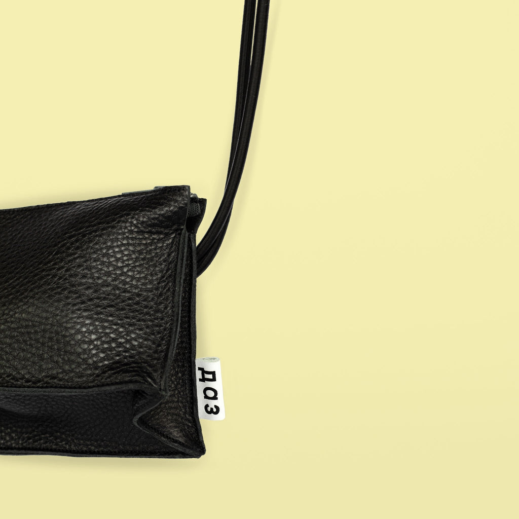 3. Close-up of Daz Studio black leather bum bag showing embossed logo on white leather tag and texture detail