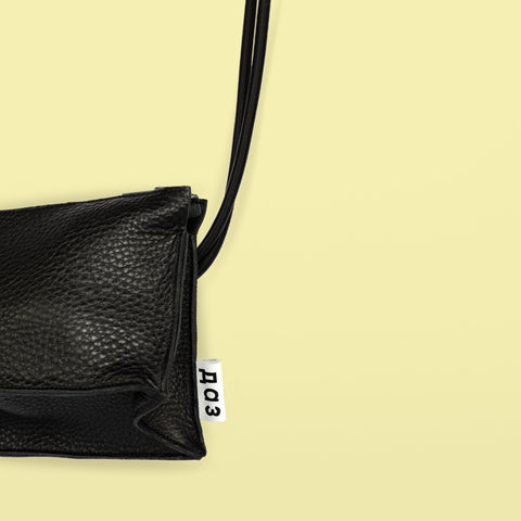 3. Close-up of Daz Studio black leather bum bag showing embossed logo on white leather tag and texture detail