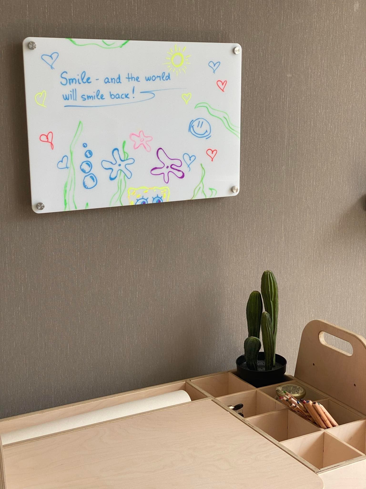 10. LUULA acrylic whiteboard mounted on wall with colorful drawings and desk below